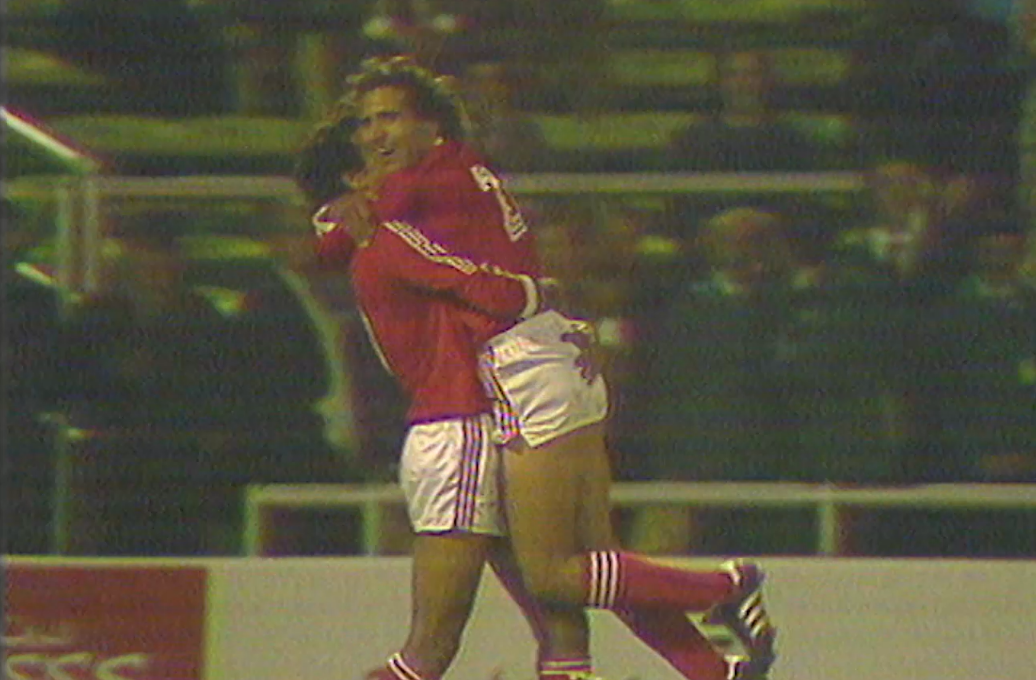 Historic Celebration: Tunisia National Football Team in Classic Match Two Tunisia national football team players in red and white kits celebrating a goal with an embrace during a historic football match.