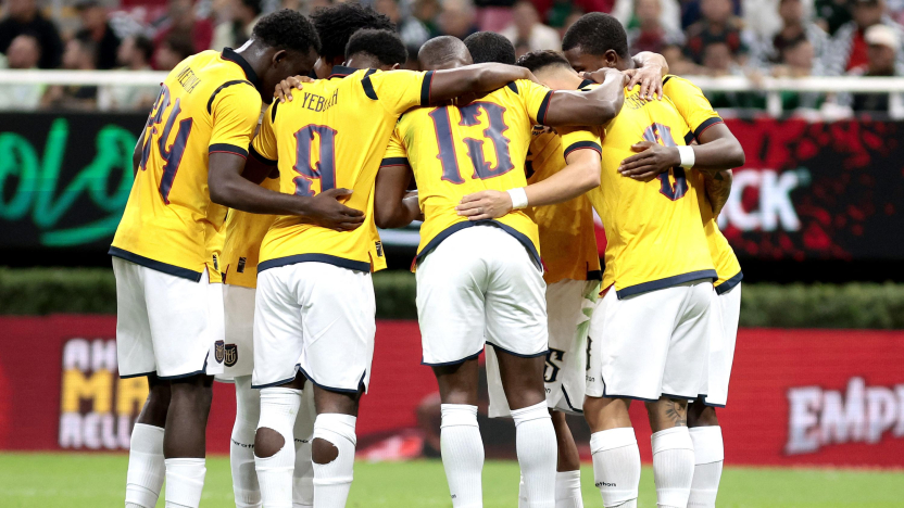 Ecuador national football team players in yellow uniforms and white shorts huddle together on the pitch during a soccer match.