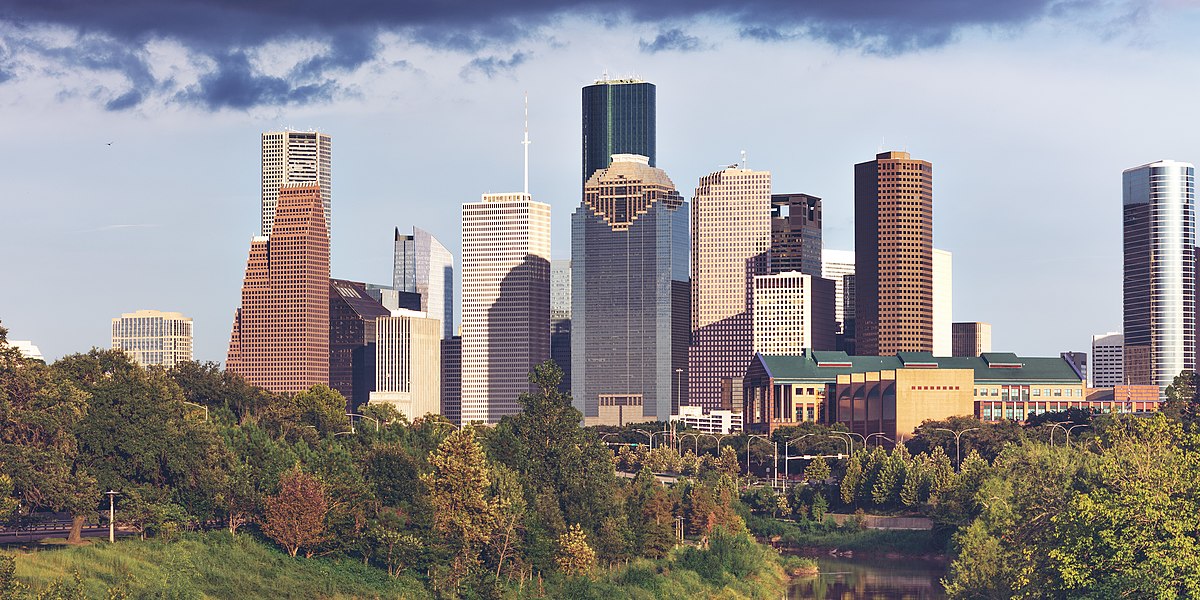 Downtown Houston Skyline with Lush Greenery in the Foreground Panoramic view of downtown Houston skyline with tall skyscrapers and green trees in the foreground under a partly cloudy sky.