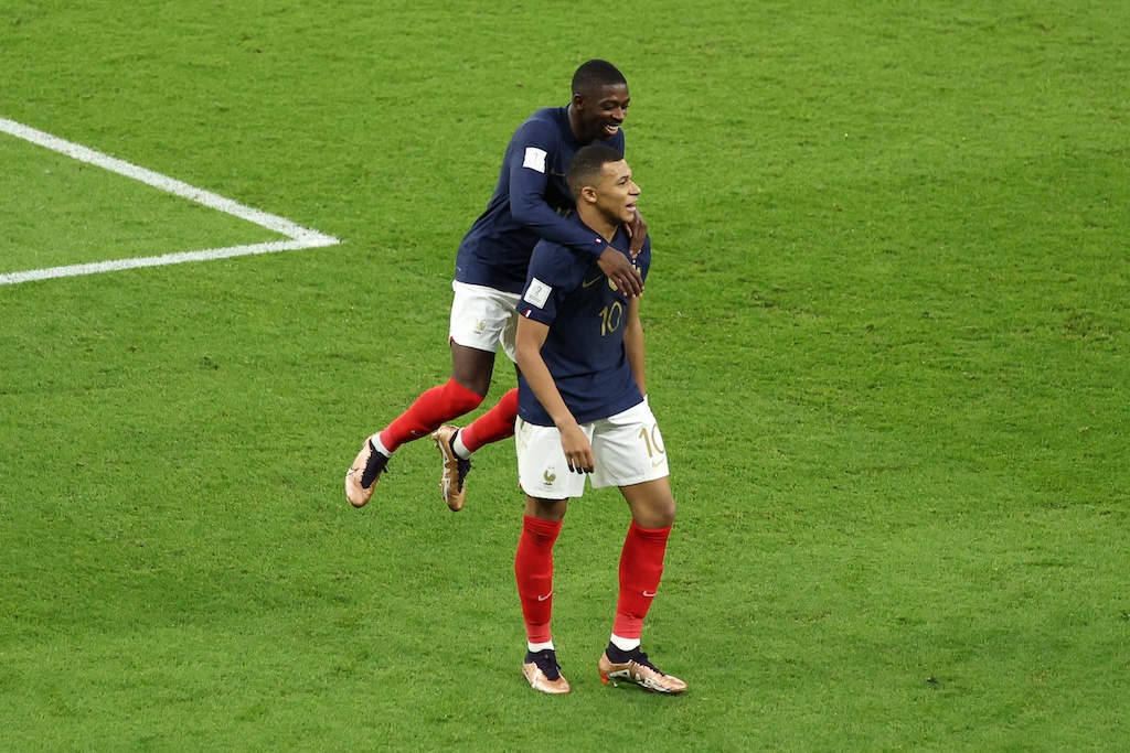 French football players in blue jerseys and red socks celebrate a goal together on the field during a World Cup match.