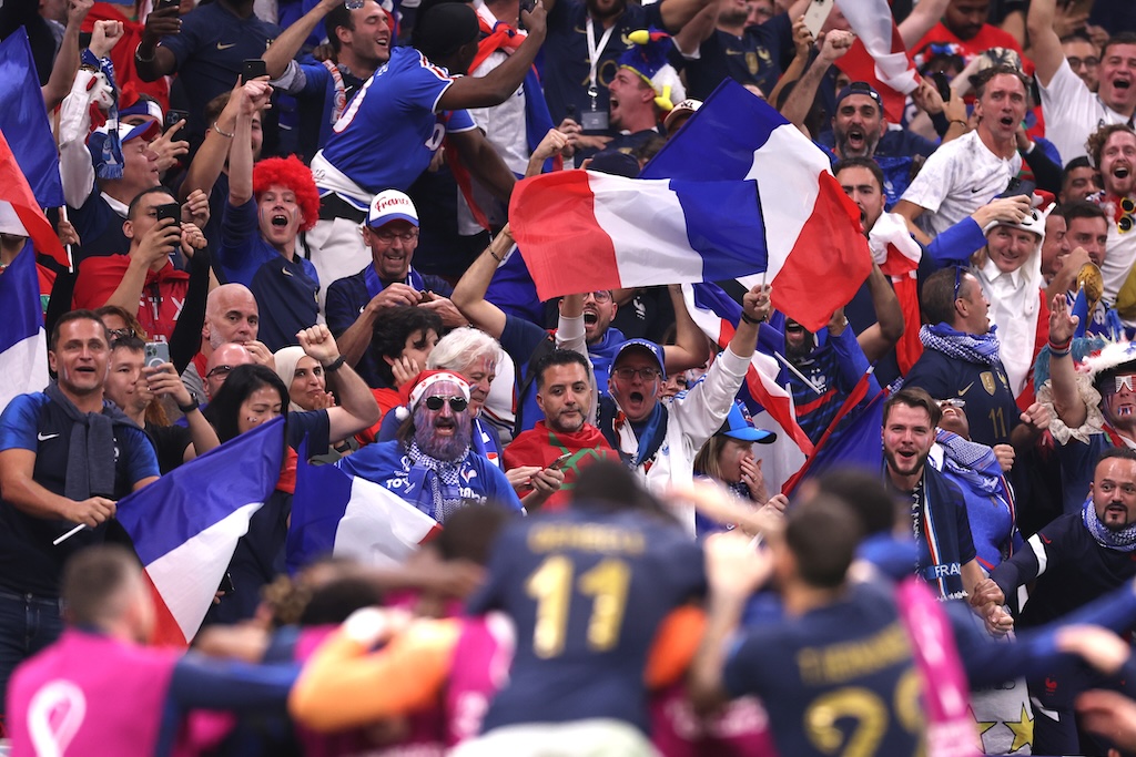 French Football Fans Celebrate in Stadium with Flags and Cheers French football fans waving flags and cheering energetically in the stadium during an international match.