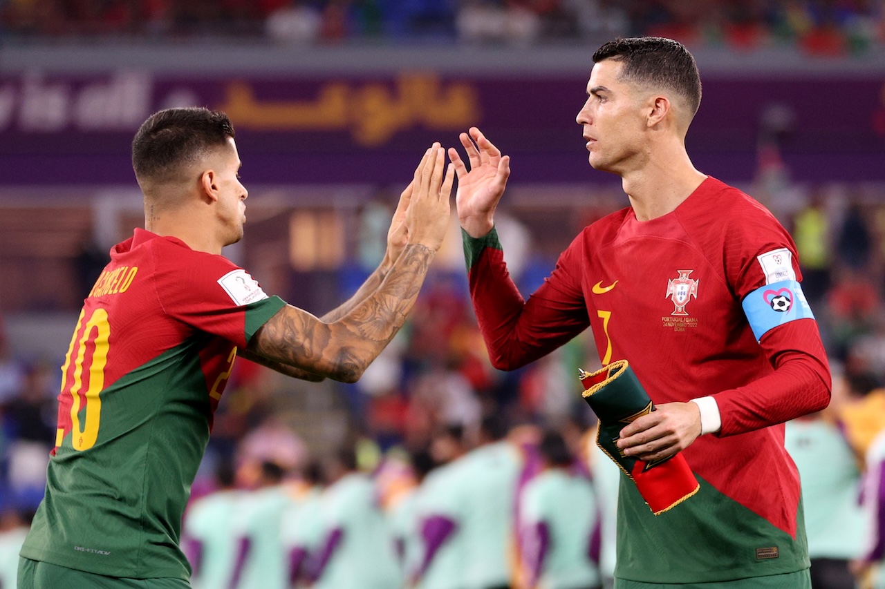 Cristiano Ronaldo and João Cancelo high-five in Portugal kit during a FIFA World Cup match.