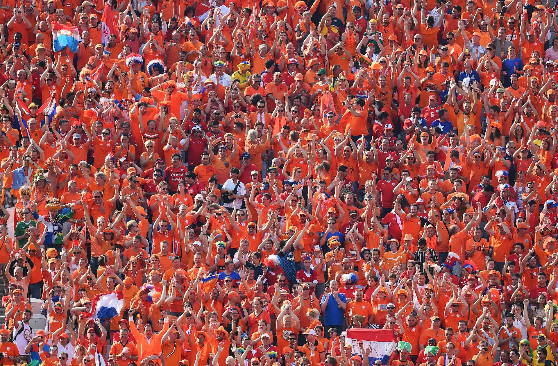 Dutch football fans in orange shirts cheering together in the stadium stands during a match.