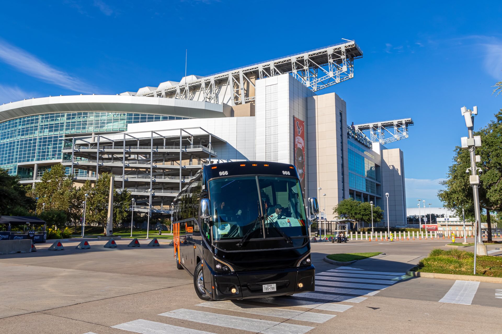 Team bus in front of NRG Stadium in Houston, Texas, with stadium structure and clear blue sky in the background.
