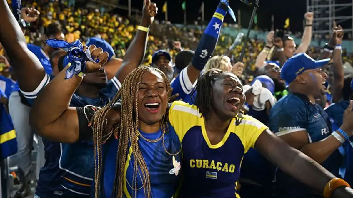 Curaçao football fans in blue and yellow shirts cheering and celebrating in the stadium stands.