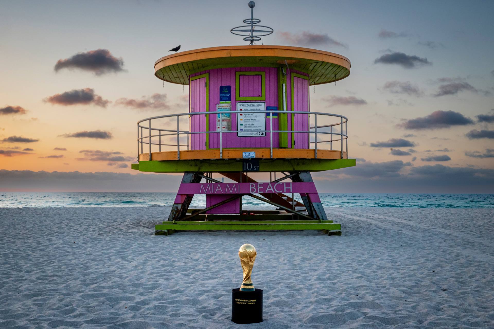 FIFA World Cup trophy on Miami Beach sand in front of the 10th Street pink lifeguard stand at sunset